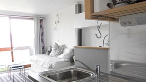 A modern kitchen with a built-in sink, a wooden shelf above the countertop, and a window with curtains.