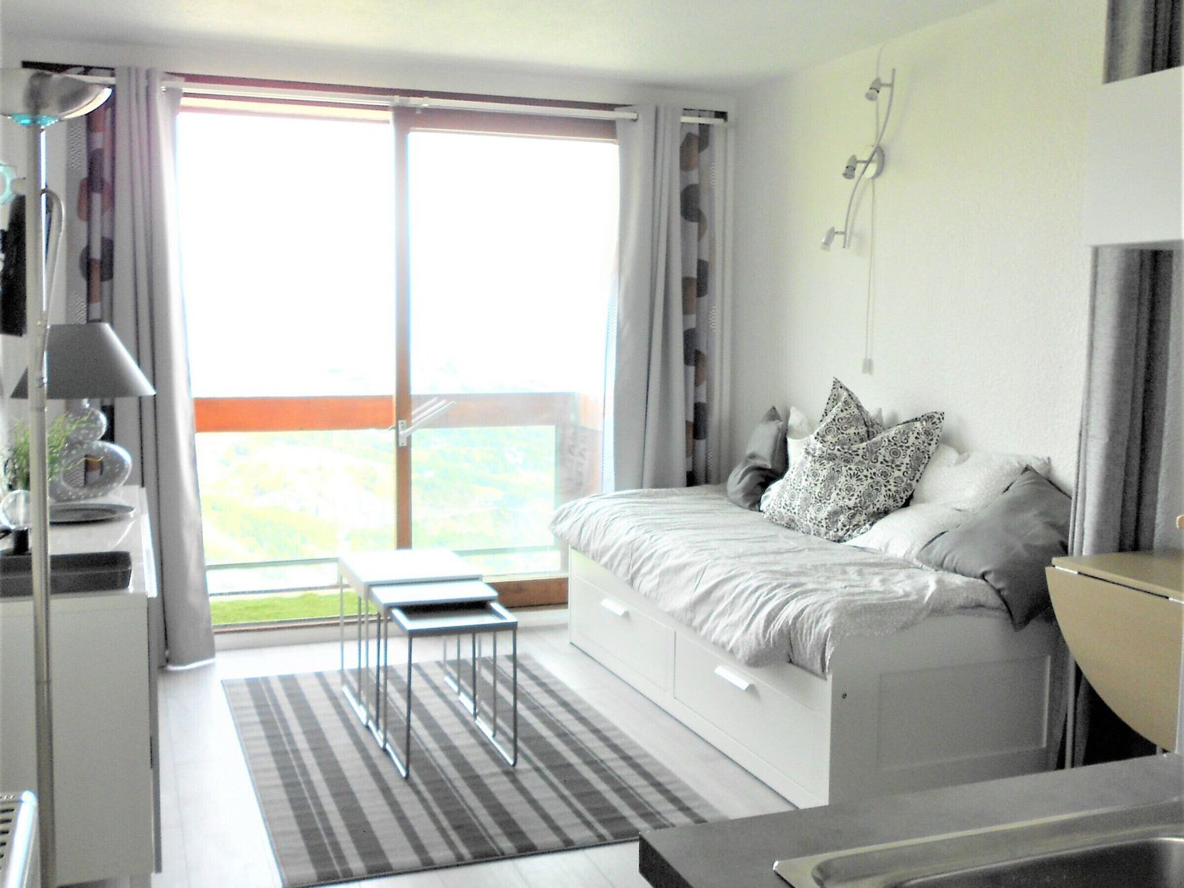 A modern bedroom with a bed, bedside table, and a view of a balcony.