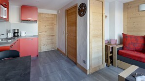 A compact living space with a kitchenette, a dining area, and a seating area with a red sofa. - Renovated studio near slopes with Mont Blanc view (La Plagne Montchavin Les Coches)