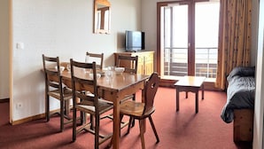 Une pièce comprenant une table à manger en bois, des chaises, un téléviseur et un lit.