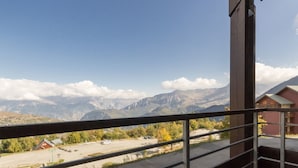 Un balcon doté d’une rambarde en métal, donnant sur un parking et un paysage montagneux.