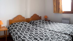 Une chambre à coucher avec un lit en bois, deux tables de chevet avec des lampes et une fenêtre avec des rideaux.