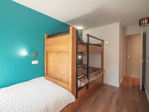 Een slaapkamer met stapelbedden, teal muren, een houten vloer en een witte dekbedovertrek.