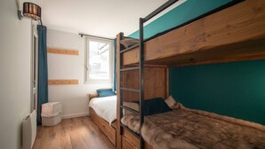 Une petite pièce avec un lit superposé, une petite fenêtre et un radiateur.