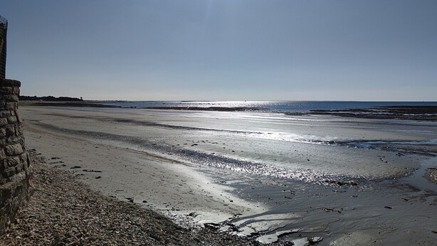 A beach with a clear sky and the sun shining.