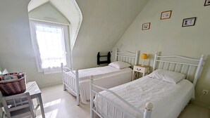 A bedroom with two beds, a window, a chair, and a bedside table.