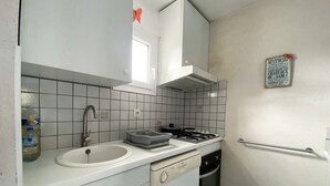 A compact kitchen with a sink, stove, and a small trash bin.