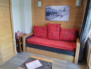 Een houten interieur met een slaapbank, een kleine tafel en een ingelijst foto aan de muur.