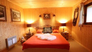 Un cuarto de madera acogedor con una cama grande, dos mesitas de noche con lámparas, un calentador y un cuadro enmarcado en la pared.