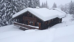 Una cabaña de madera con un techo cubierto de nieve, rodeada de árboles cargados de nieve.