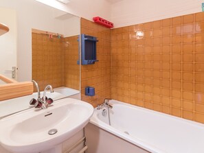Ein Badezimmer mit einem weißen Waschbecken, einer Badewanne und einem Spiegel. An der Wand hängt ein roter Korb und ein blauer Seifenspender steht bereit.