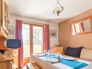A room with a bed, a table set for dining, a television, and a window with curtains.