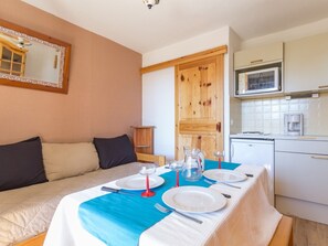 A room with a bed, a dining table set for two, a kitchen area with a microwave, and a wooden door. - Bright 2-room apartment near slopes, free WIFI (La Rosière)