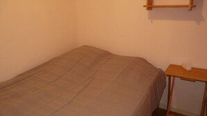 Una stanza piccola con un letto singolo, un comodino in legno e una presa di corrente.