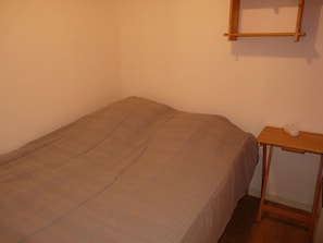 A small, single-bed room with a wooden nightstand and a power outlet.
