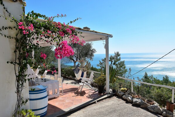 A terrace with a white pergola, white chairs, a table, and a large barrel.