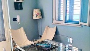 A room with a glass-top table, two white chairs, a lamp, a clock, and a window with blinds. - - Gli Orizzonti di Agata - Villa with a wide view of the sea - MARGHERITA - (Puglia)