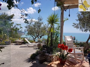 A patio with a white chair, potted plants, and a view of the sea.