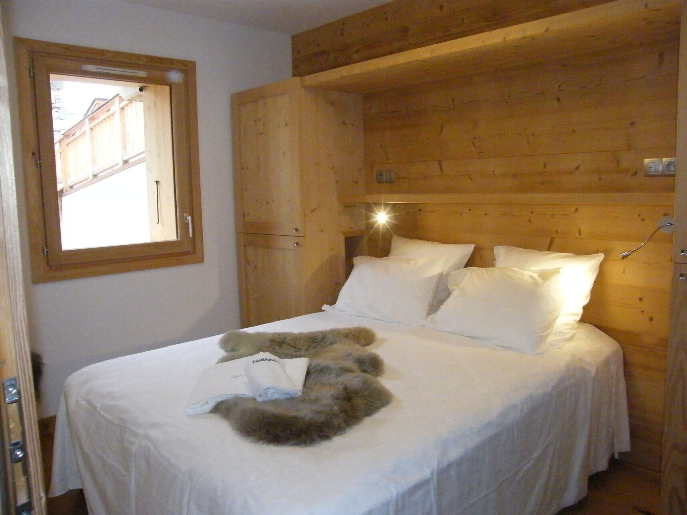 Een slaapkamer met houten lambrisering, een bed, een raam en een kledingkast.