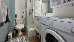 Een kleine badkamer met toilet, douche en wasmachine.