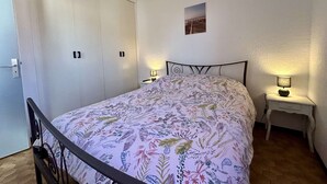 Een slaapkamer met een bed, een kledingkast, een nachtkastje en een klein schilderij aan de muur.