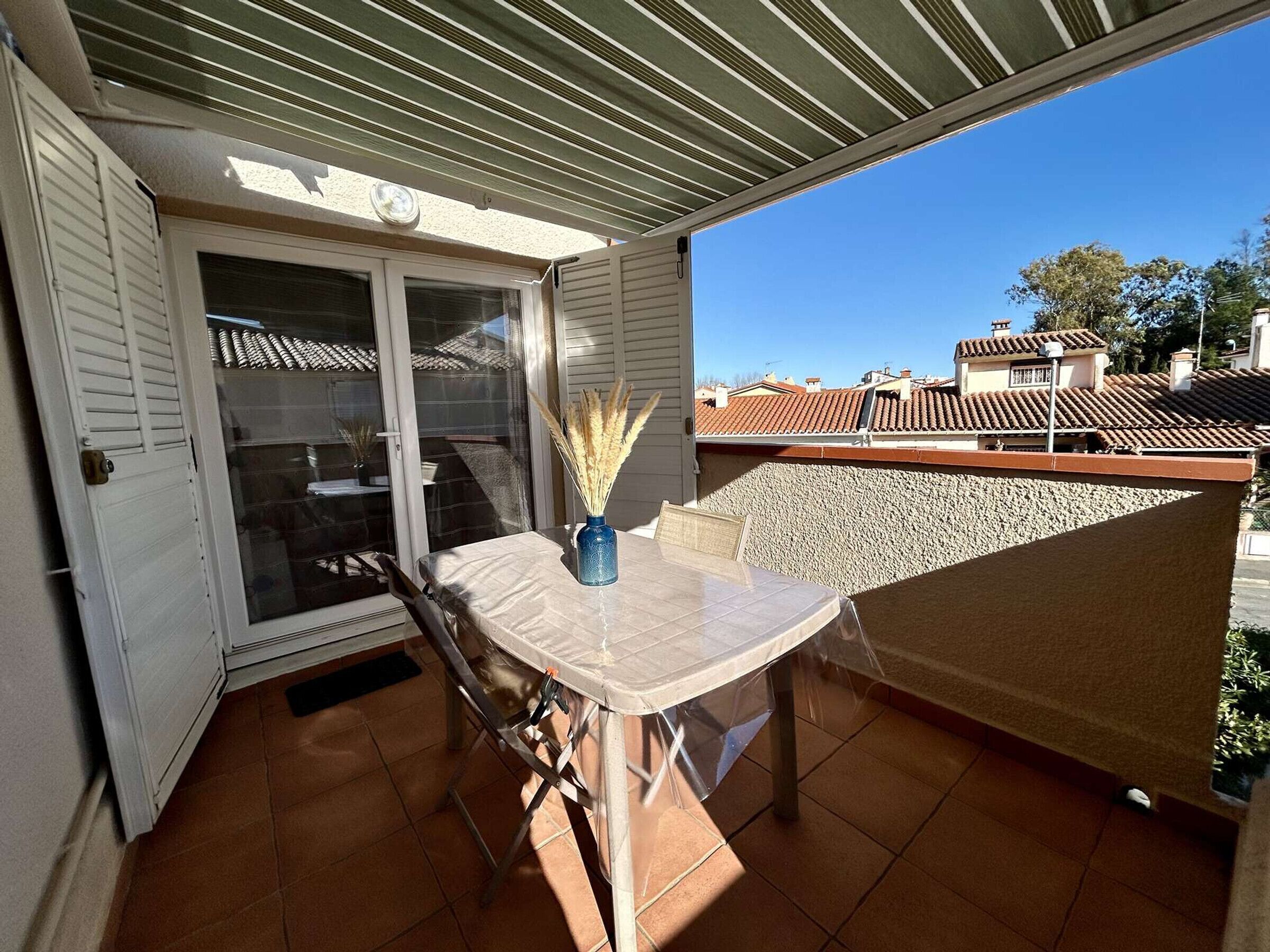 Un balcon avec une table et des chaises, une porte-fenêtre coulissante et une vue sur les bâtiments voisins.