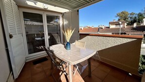 Een balkon met een tafel, stoelen, een schuifdeur en uitzicht op omliggende gebouwen.
