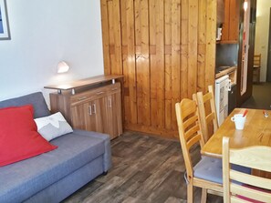 A compact living space with a sofa, wooden cabinets, a dining table, and a kitchenette.