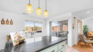 A modern kitchen with a large island, pendant lights, and a view of the outdoors.