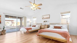 A bedroom with two beds, a ceiling fan, and a large window.