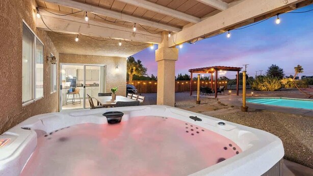 An outdoor hot tub area with a covered patio, a pool, and a gazebo.