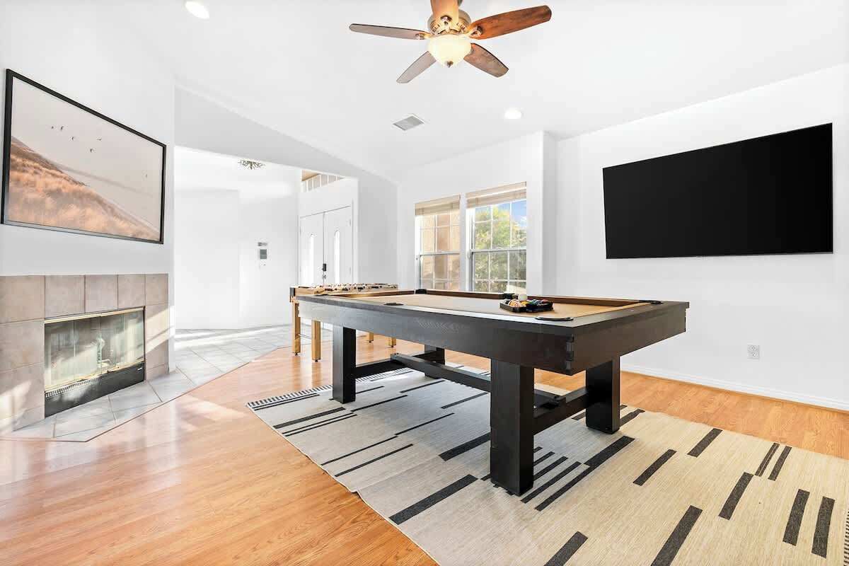 A modern living room with a pool table, a fireplace, and a large TV on the wall.
