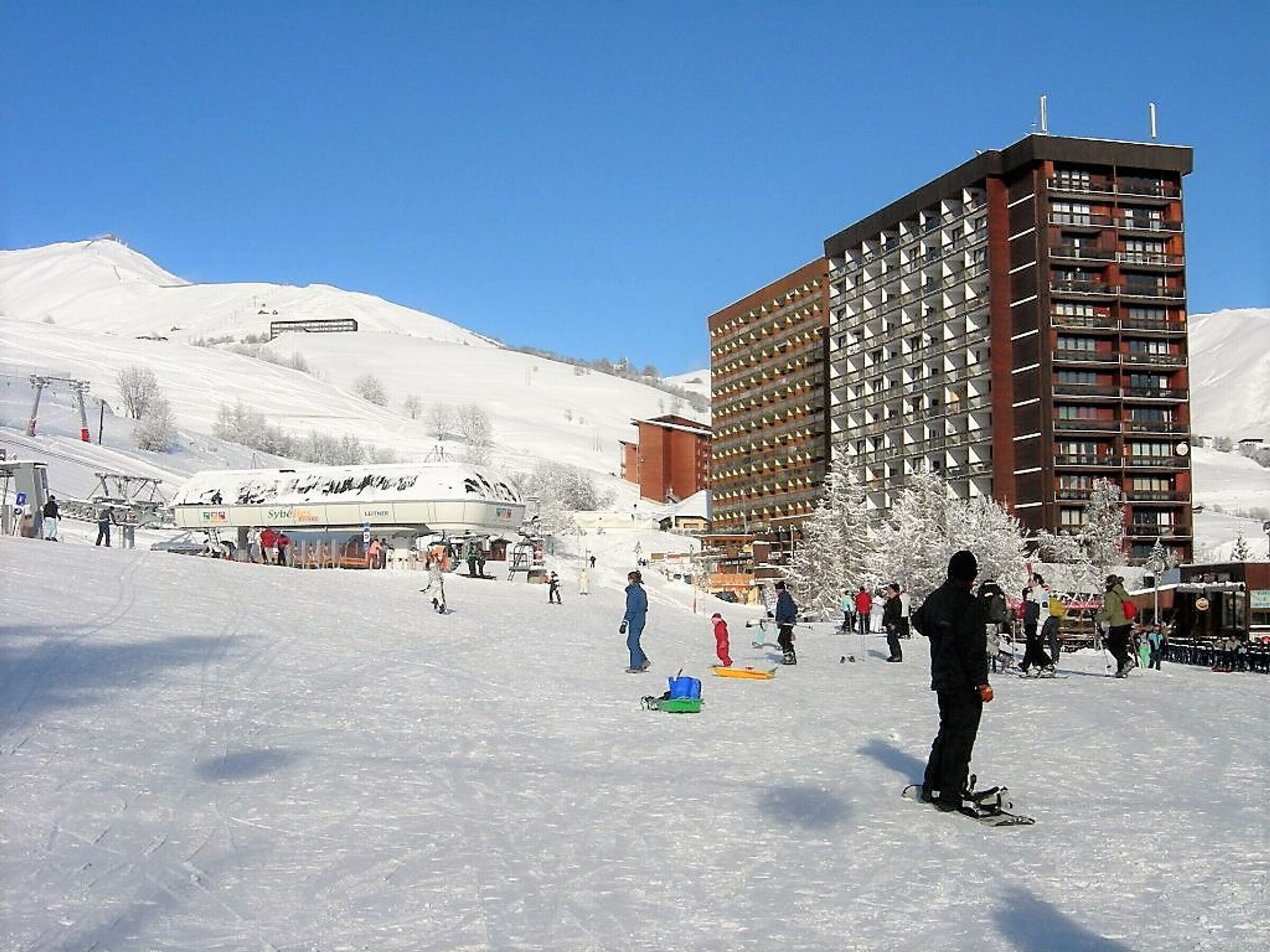Une station de ski avec un grand bâtiment, probablement un hôtel, comprenant plusieurs étages et des balcons.