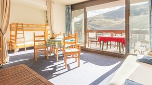 A room with a bunk bed, a dining table with chairs, a balcony with a table and chairs, and a large window with a view of the countryside. - Bright studio in Le Corbier, balcony, 4 pers (Le Corbier)