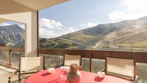 A dining area with a red table, chairs, and a view of a mountainous landscape. - Bright studio in Le Corbier, balcony, 4 pers (Le Corbier)