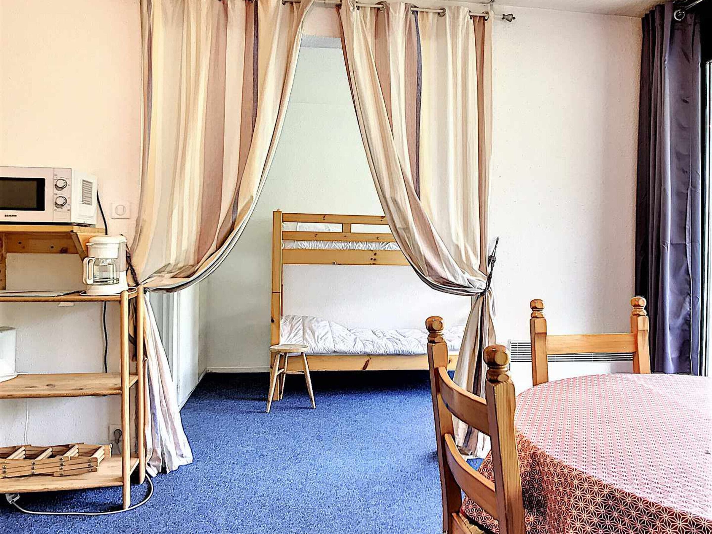 A room with a bunk bed, a desk with a microwave, a chair, and a shelf with a coffee maker.