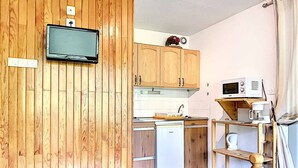 A compact kitchen with wooden cabinets, a microwave, a coffee maker, and a small table. - Bright studio in Le Corbier, balcony, 4 pers (Le Corbier)