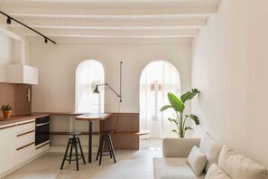 Una cocina moderna con armarios blancos, una zona de comedor con taburetes y una planta grande.