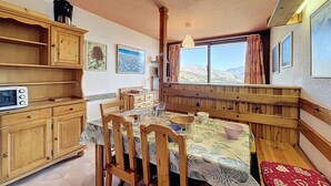 Uma sala de jantar acolhedora com móveis de madeira, uma mesa posta para quatro pessoas e uma janela com vista para as montanhas.