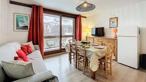 Una sala de estar acogedora con sofá, mesa de comedor y sillas. Hay un televisor, un refrigerador y una ventana con cortinas.
