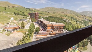 Un hotel con un edificio moderno, zona de estacionamiento y vistas a colinas y montañas verdes.
