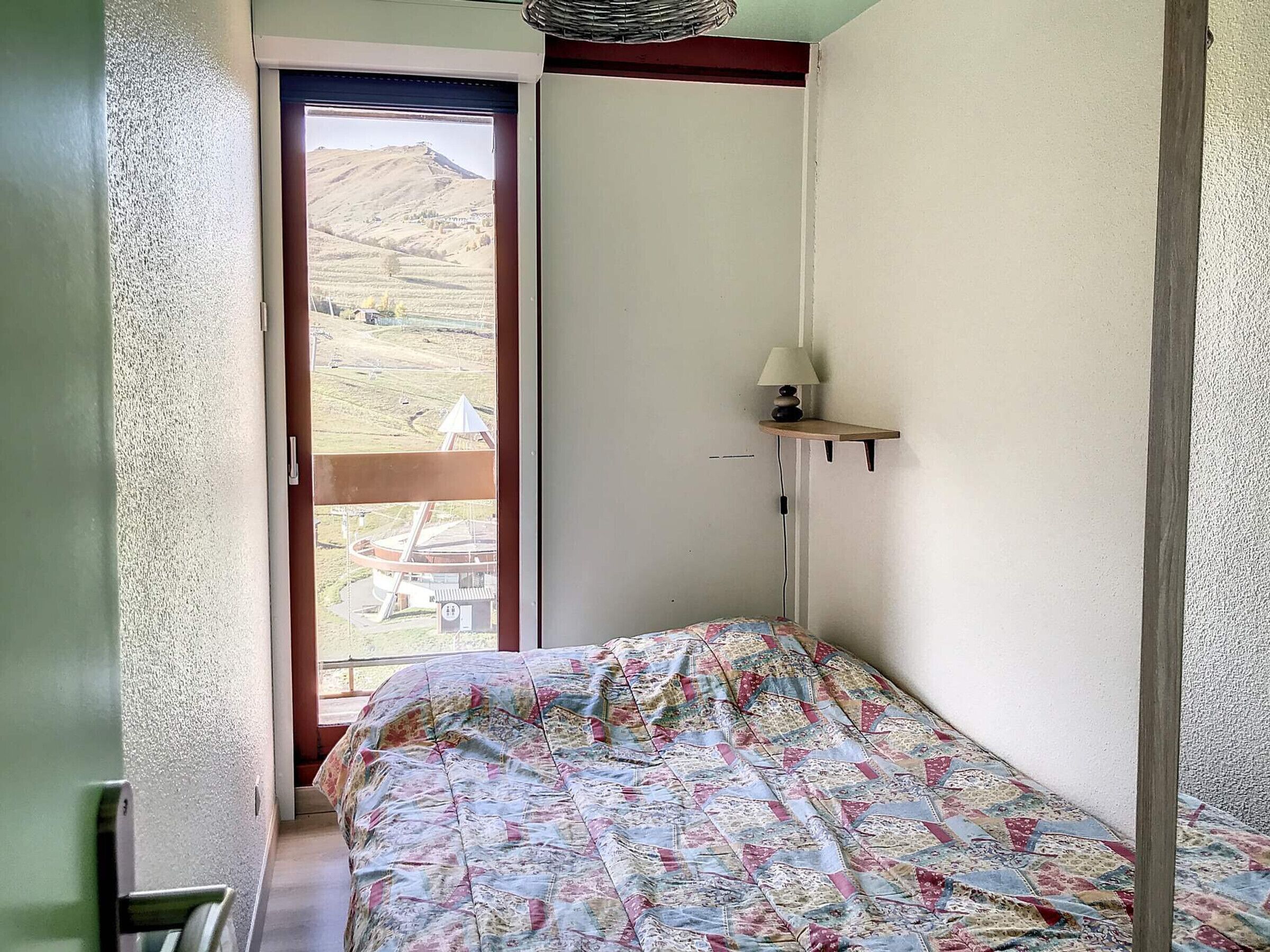 A small bedroom with a bed, a window, and a wall-mounted lamp.