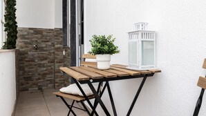 Een klein terras met een houten tafel, een plant in pot en een witte lantaarn.