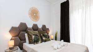 Een moderne slaapkamer met een geometrisch hoofdeinde, een ronde wanddecoratie, een nachtkastje met een lamp en een netjes opgemaakt bed met handdoeken.