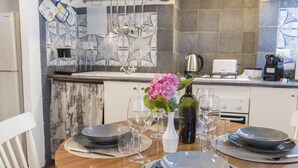 A dining table set with plates, glasses, and cutlery, a vase with flowers, and a bottle of wine in a kitchen with a tiled backsplash and modern appliances. - [Trastevere] Cozy & Charme Apartment in Rome (Roma)