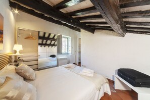 A bedroom with a large bed, a bedside table with a lamp, a dresser, a mirror, and a suitcase on a shelf. - [Trastevere] A cozy and charming apartment in Rome (Roma)