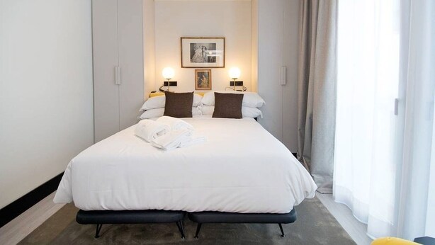 Ein Hotelzimmer mit einem großen Bett, zwei Nachttischlampen, einem gerahmten Bild an der Wand und einem Fenster mit Vorhängen.