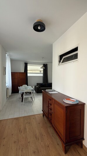 Um quarto com um armário de madeira, uma mesa de jantar com cadeiras, um sofá e uma janela com cortinas.