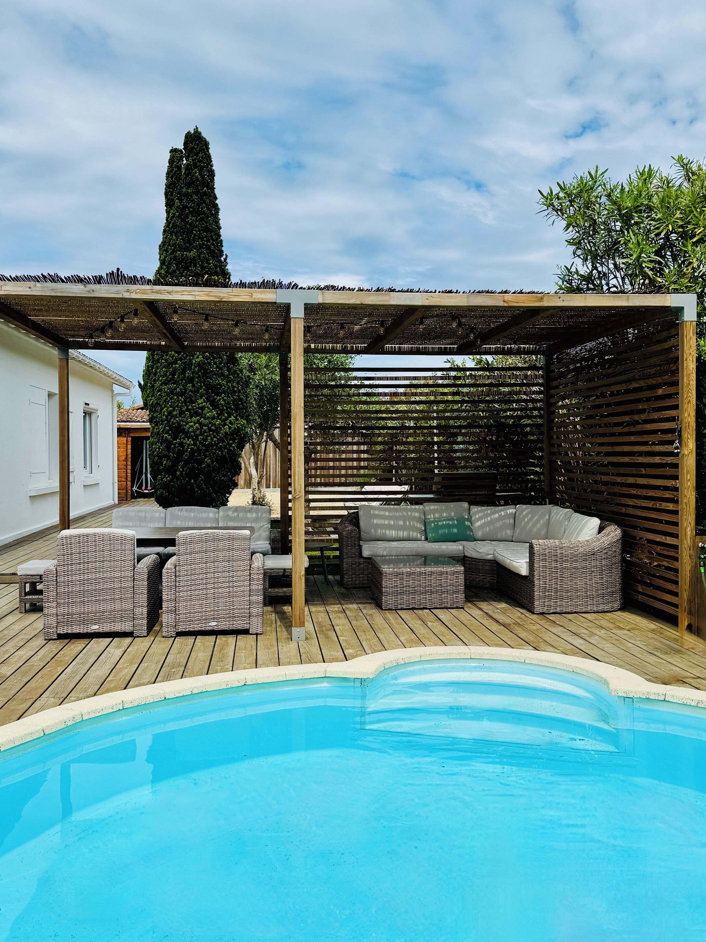 Un espacio al aire libre techado con piscina, mobiliario de mimbre y una pérgola.