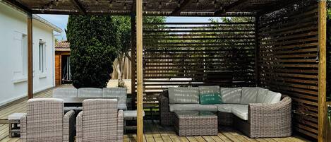 Un espacio al aire libre techado con piscina, mobiliario de mimbre y una pérgola.